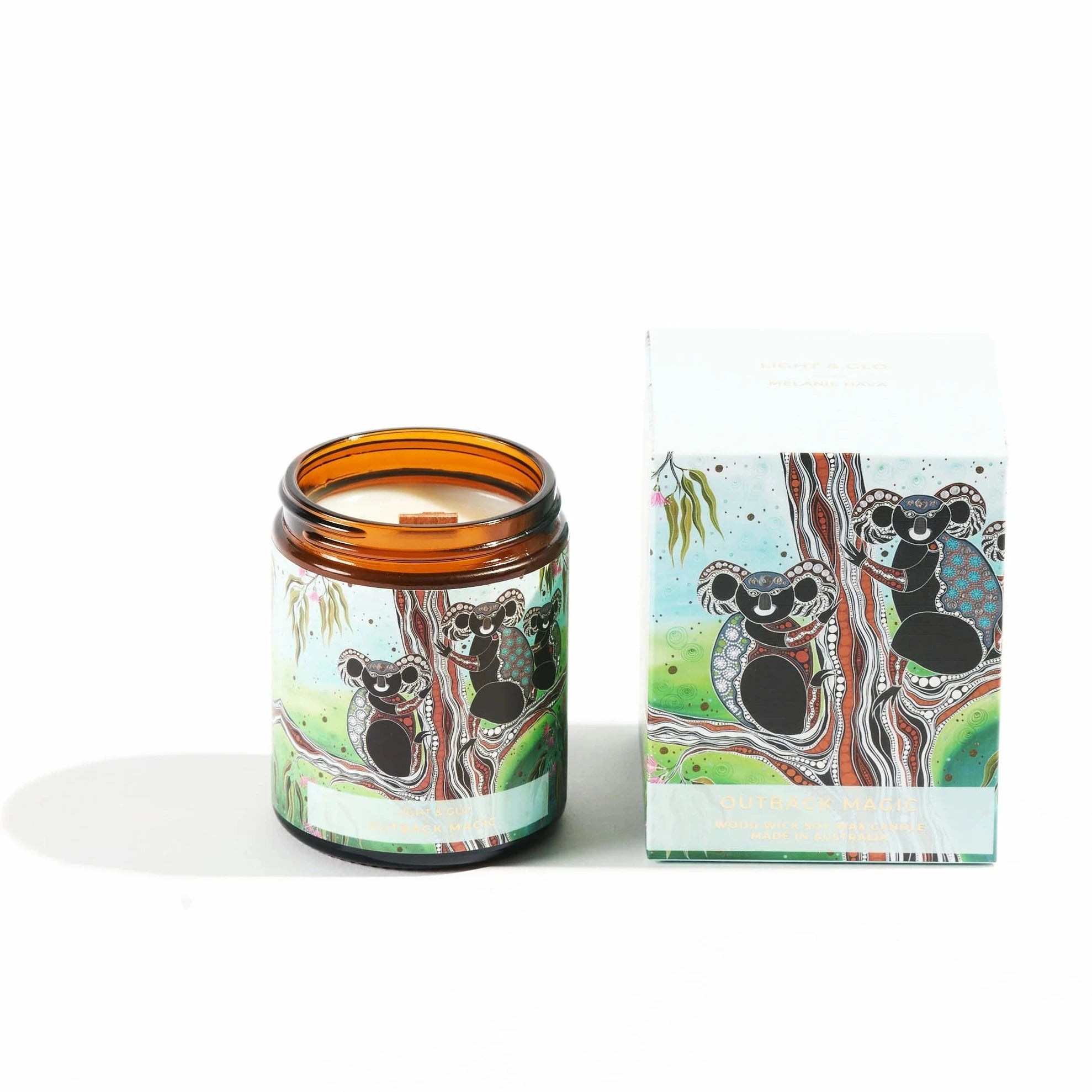 Candle in brown jar with aborigial design koala lable sitting next to gift box with the same koala print.