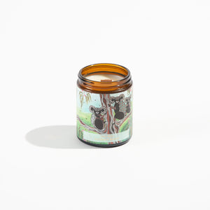 Candle in brown jar with Aboriginal koala image on the front and the lid is off.