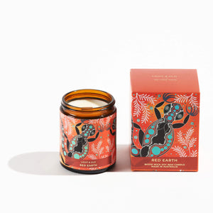 candle in brown glass jar with  aboriginal gecko design next to gift box with the same design