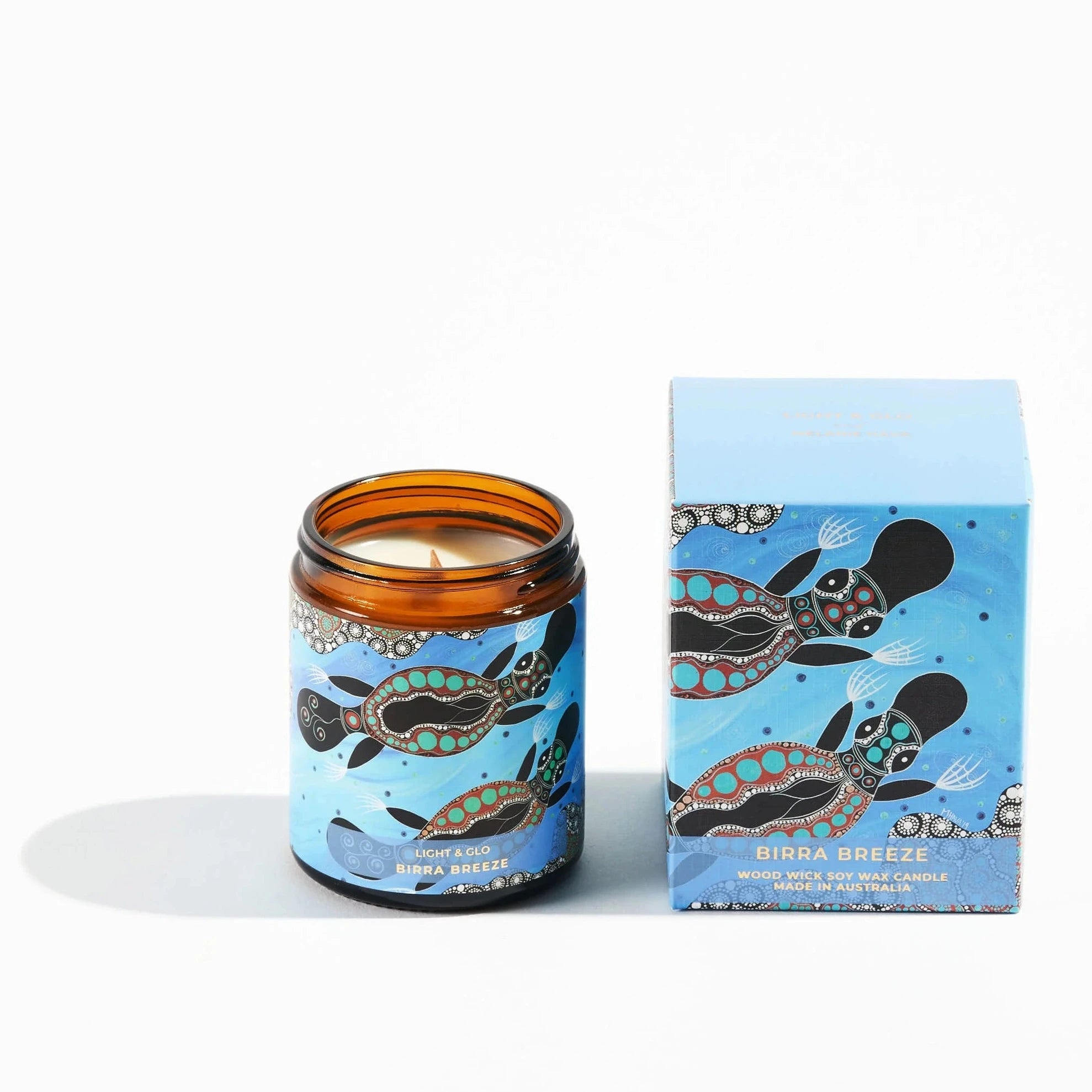 Candle in brown jar with platypus aboriginal design on label sitting next to a gift box with the same design.