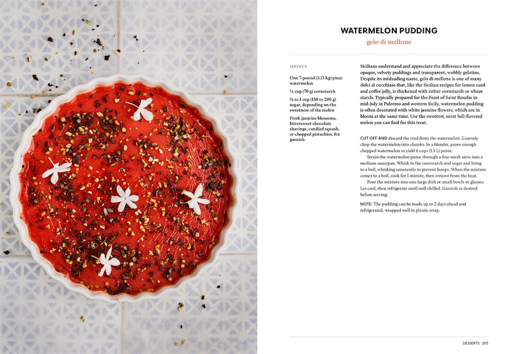 Watermelon pudding garnished with white flowers and nuts, beside a printed recipe on a patterned surface.