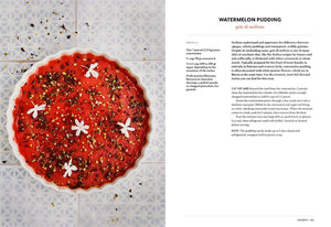 Watermelon pudding garnished with white flowers and nuts, beside a printed recipe on a patterned surface.