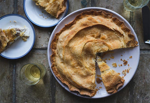 Partially eaten pie on a plate with a slice removed, next to a smaller plate with pie and two glasses of drink.