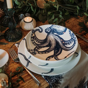 Ceramic bowl with blue octopus illustration on matching plate, styled with greenery and candles on rustic wooden table.