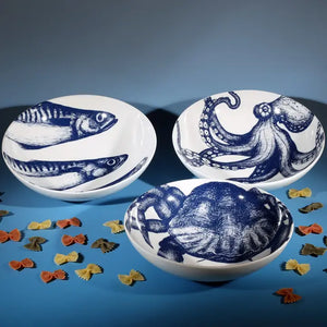White bowl with blue octopus illustration, part of sea creature set, styled on blue background with scattered pasta.
