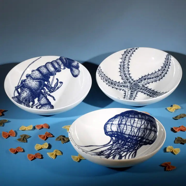 White bowl with blue lobster illustration, part of sea creature set, styled with colourful pasta for coastal kitchen decor.