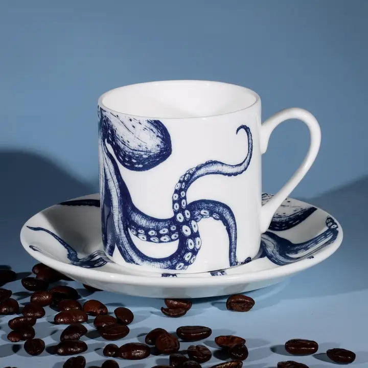 White espresso cup and saucer with blue octopus design, styled with coffee beans on light blue background for coastal decor.