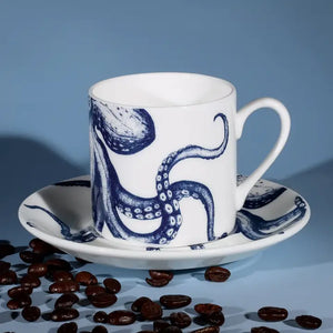 White espresso cup and saucer with blue octopus design, styled with coffee beans on light blue background for coastal decor.