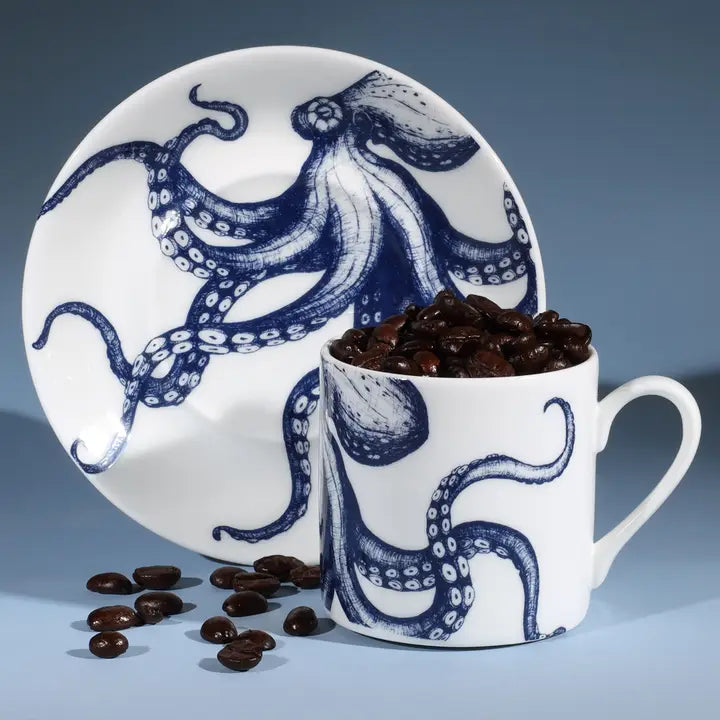 White espresso cup and saucer with blue octopus design, filled with coffee beans, styled on a blue background.