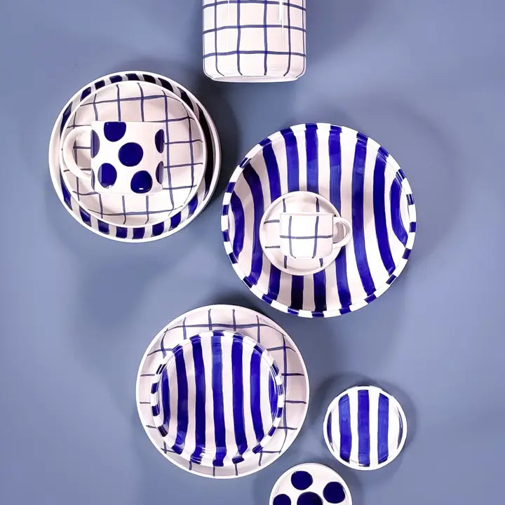 White ceramic dishes with blue stripes, polka dots, and grid patterns, arranged neatly on a blue background.