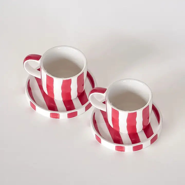 Two white ceramic cups with vertical red stripes on matching saucers with horizontal red stripes, on white surface.