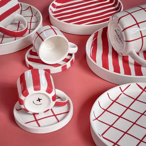 Red and white striped and checkered ceramic mugs and plates, arranged on a pink background.