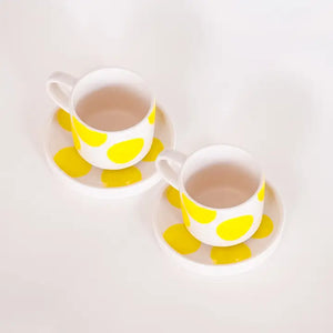 Two white ceramic espresso cups with matching saucers, decorated with bold yellow hand-painted dots.