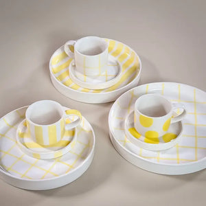 Set of three white ceramic espresso cups with matching saucers and plates, featuring hand-painted yellow dots, stripes, and grids.