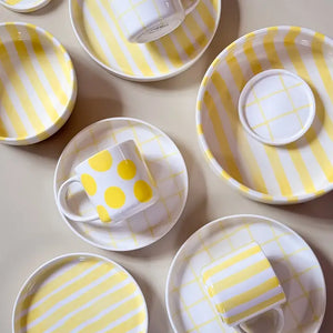Yellow and white ceramic cup and saucer with polka dot pattern, displayed on a beige surface.