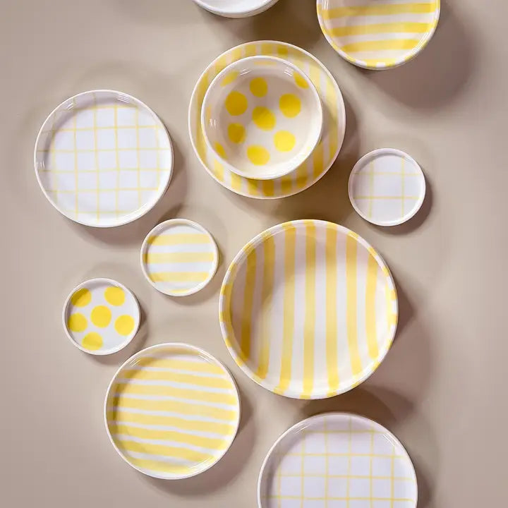 Ceramic bowls and plates with yellow stripes, grids, and polka dots, arranged neatly on a beige surface.