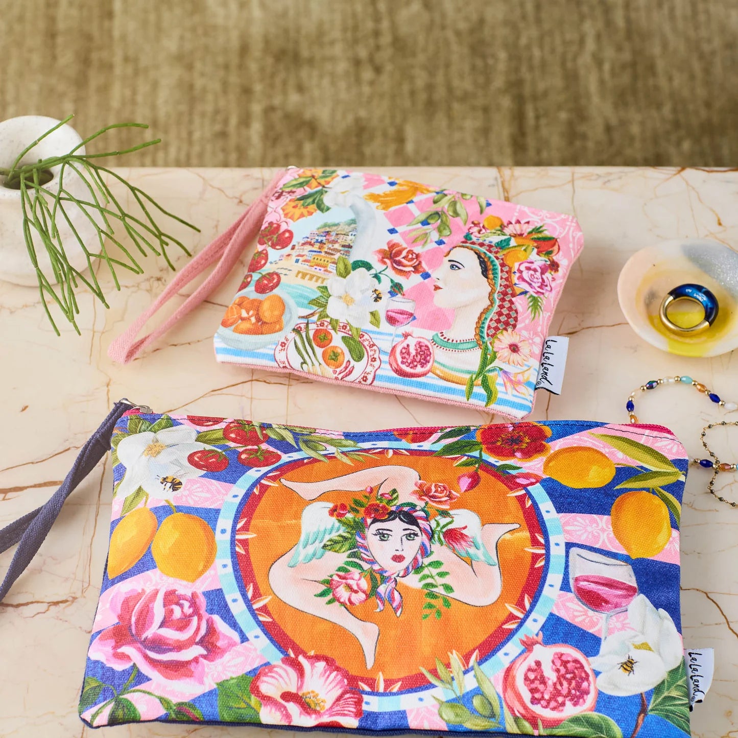 Two Italian summer coin purses with vibrant designs of women, fruits, flowers, and scenic coastal elements.