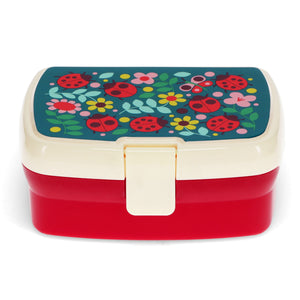 Front view image of red and white lunch box with image of ladybirds and flowers on the top on white background.