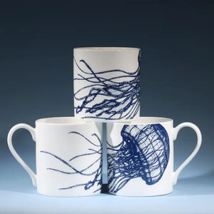 White ceramic mugs with blue jellyfish design stacked in pyramid shape on dark background.