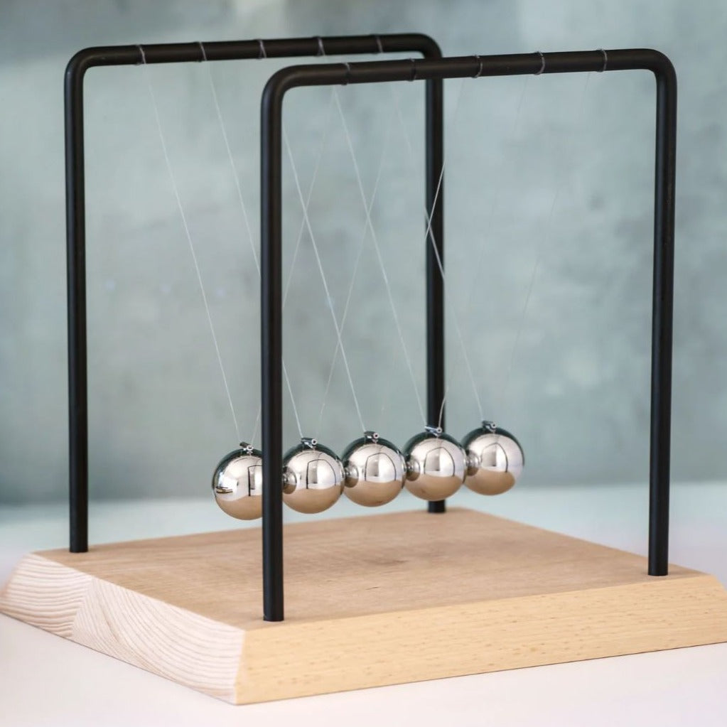 Image of 18cm Tall Newtons Cradle on white surface with grey wall behind