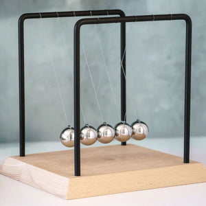 Image of 18cm Tall Newtons Cradle on white surface with grey wall behind
