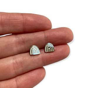 Front view image of silver stud earring in rainbow shape between someone's fingers for size