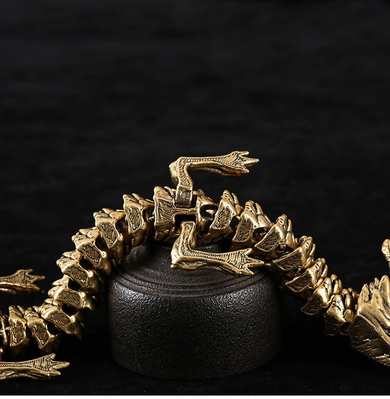 Close-up of a gold-colored dragon figurine with detailed segments and clawed limbs, coiled around a black cylindrical stand on a textured black surface.