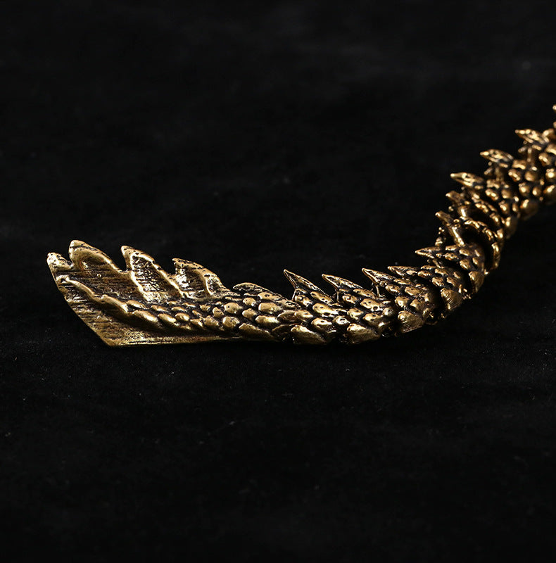 Close-up of a dragon figurine’s tail with detailed scales and spikes, finished in metallic gold. Set against a black background for contrast.