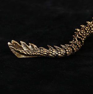 Close-up of a dragon figurine’s tail with detailed scales and spikes, finished in metallic gold. Set against a black background for contrast.