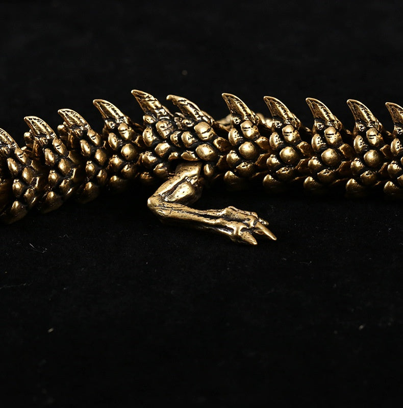Close-up of a gold dragon figurine with detailed scales and sharp claws. One leg with three claws is prominently visible, set against a black background.