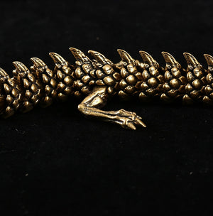 Close-up of a gold dragon figurine with detailed scales and sharp claws. One leg with three claws is prominently visible, set against a black background.