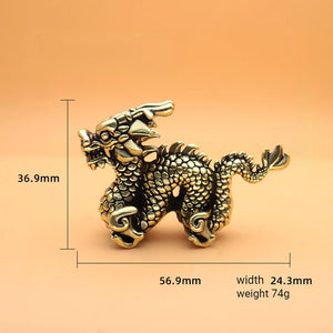A small metallic dragon figurine with intricate detailing, including scales and curled limbs, displayed against a warm orange background. The dimensions are labeled: height 36.9 mm, length 56.9 mm, width 24.3 mm, and weight 74g.
