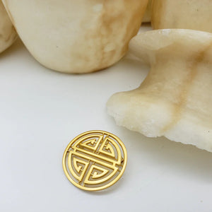 Image of Shou symbol brooch, round gold cut out symbol on white  and stone background.