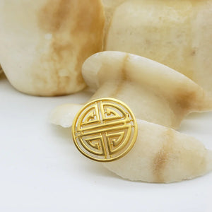 Image of Shou symbol brooch, round gold cut out symbol on white and stone background.
