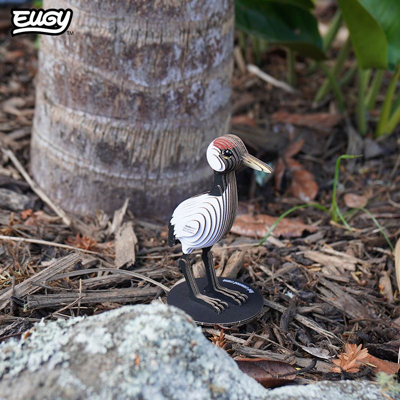Image of EUGY Crane showing 3D carboard model of a red-crowned crane with white body, black neck and legs, and a red patch on the head on wood mulch.
