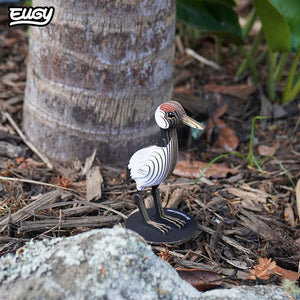 Image of EUGY Crane showing 3D carboard model of a red-crowned crane with white body, black neck and legs, and a red patch on the head on wood mulch.