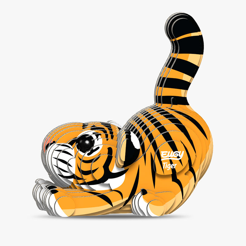 Side view image of Eugy Tiger, showing tiger model made form layers of cardboard in orange, black and white. Models paws are stretched out in front with bottom in the air and tail sticking up. White background.