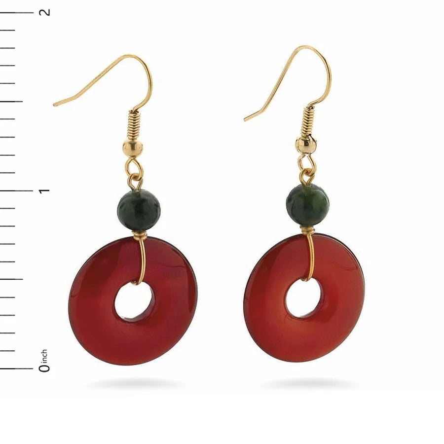 Image of gold pendant earrings with green bead and red bi disc on white background.