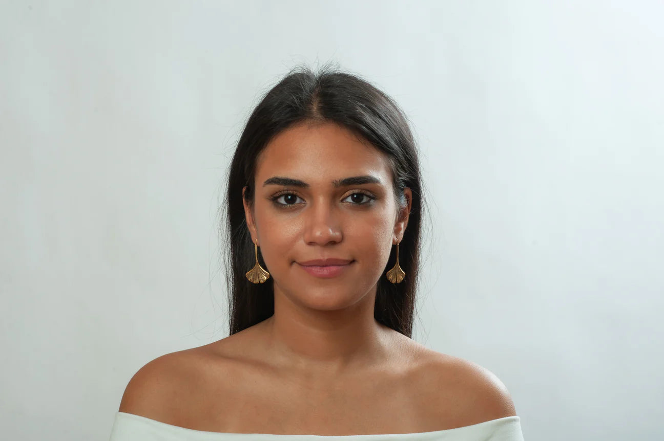 Image of girl with dark hair wearing ginkgo leaf shaped drop earrings in gold finish on white background.