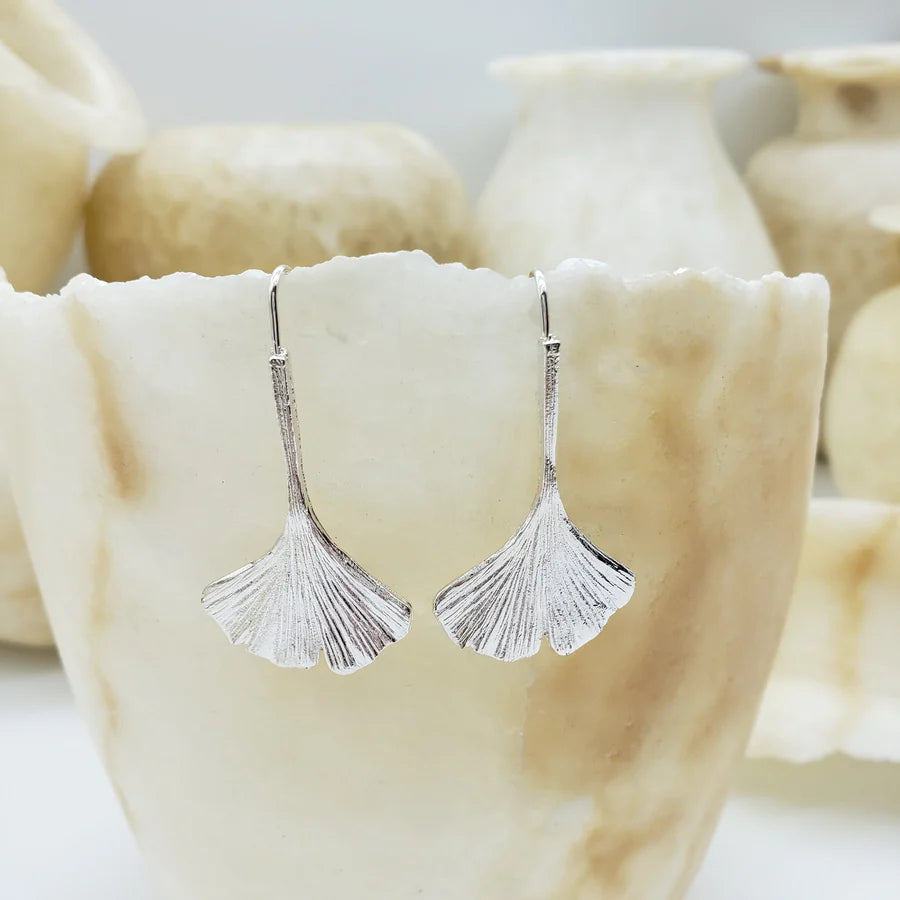 Image of ginkgo leaf shaped silver drop earrings hanging on piece of stone.
