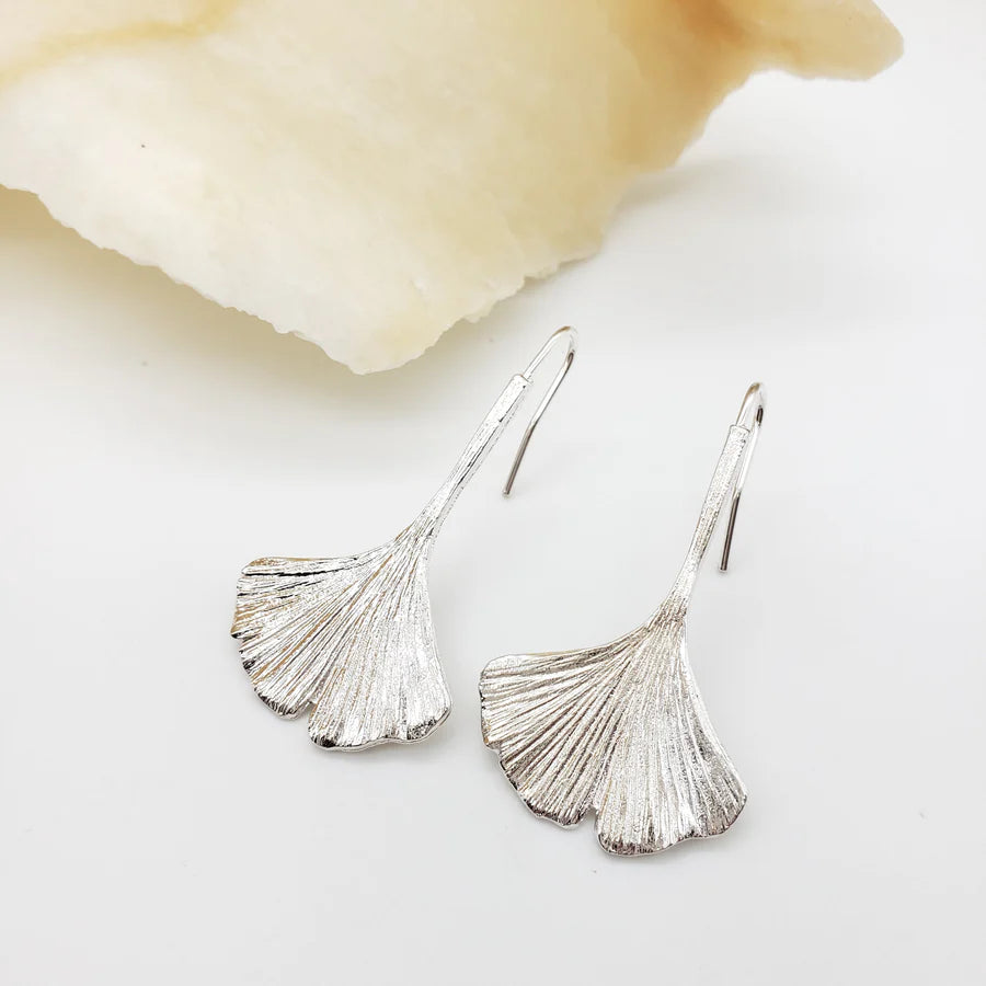 Image of ginkgo leaf shaped silver drop earrings on white and stone background.