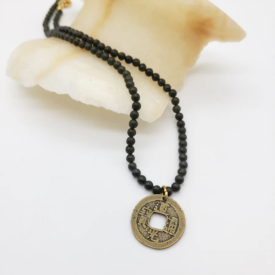Image of Chinese coin pendant on dark green jade bead necklace on white background.
