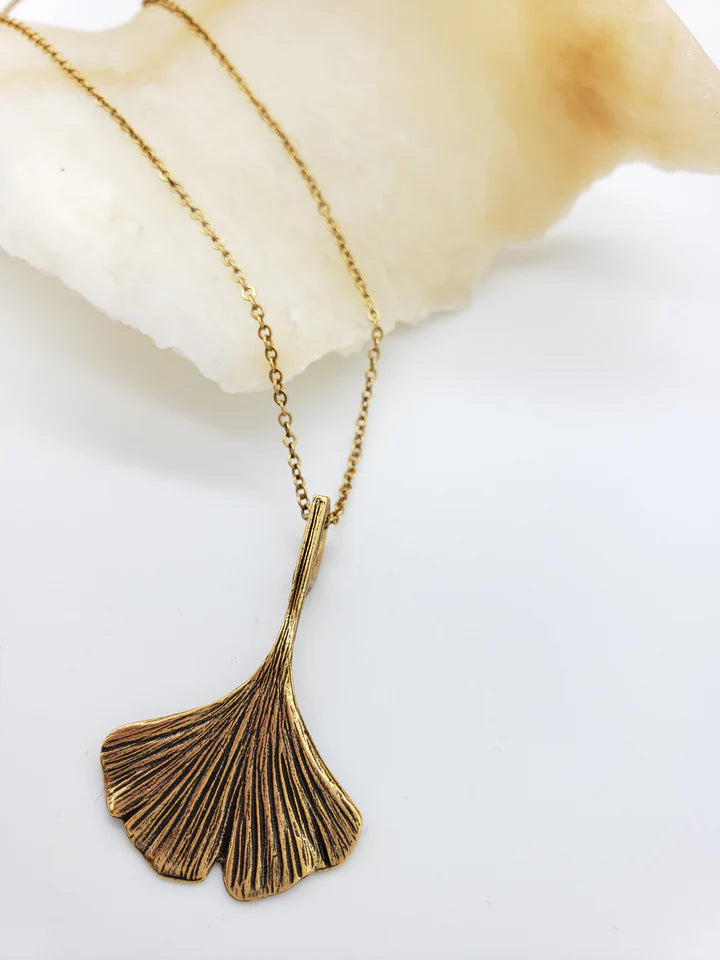 Image of ginko leaf shaped pendant in antique gold on gold chain, on white background.