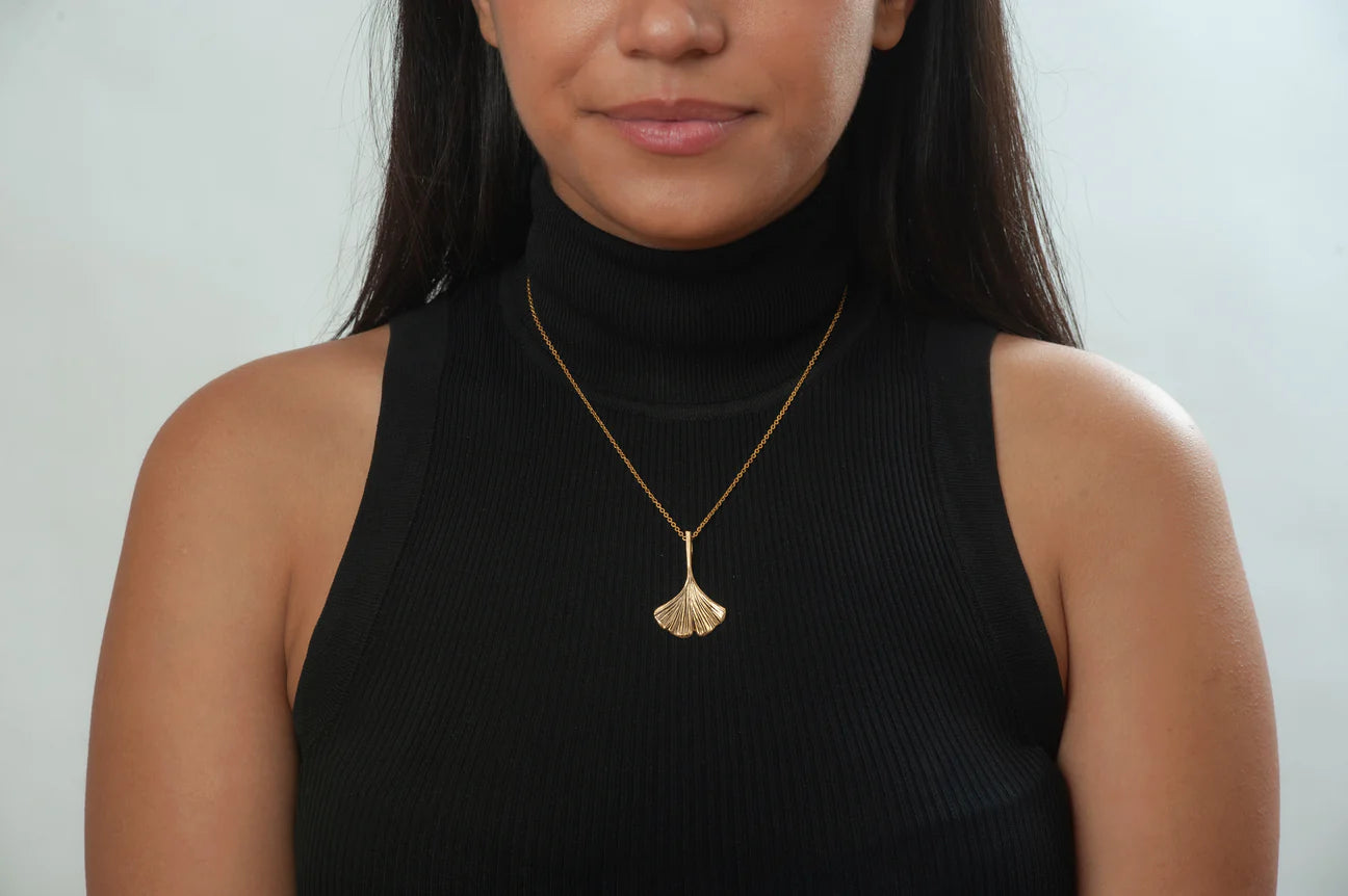 Image of girl with black top wearing ginko leaf shaped pendant on gold chain.