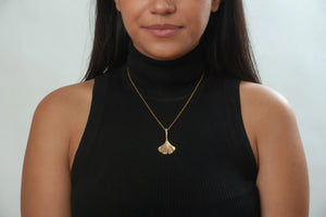 Image of girl with black top wearing ginko leaf shaped pendant on gold chain.
