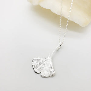 Image of ginko leaf shaped silver pendant on silver chain on white background.