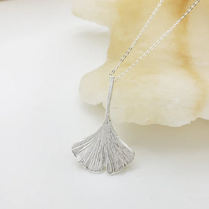 Image of ginko leaf shaped silver pendant on silver chain on white background.