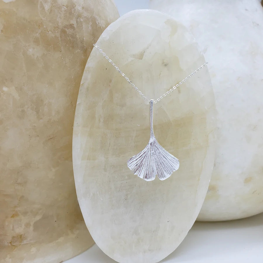 Image of ginko leaf shaped silver pendant on silver chain hanging on white crystal.