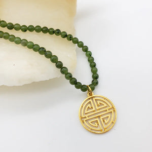 Image of gold Shou symbol pendant on necklace of green beads hanging on white background.