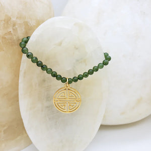 Image of gold Shou symbol pendant on necklace of green beads hanging on white crystal.